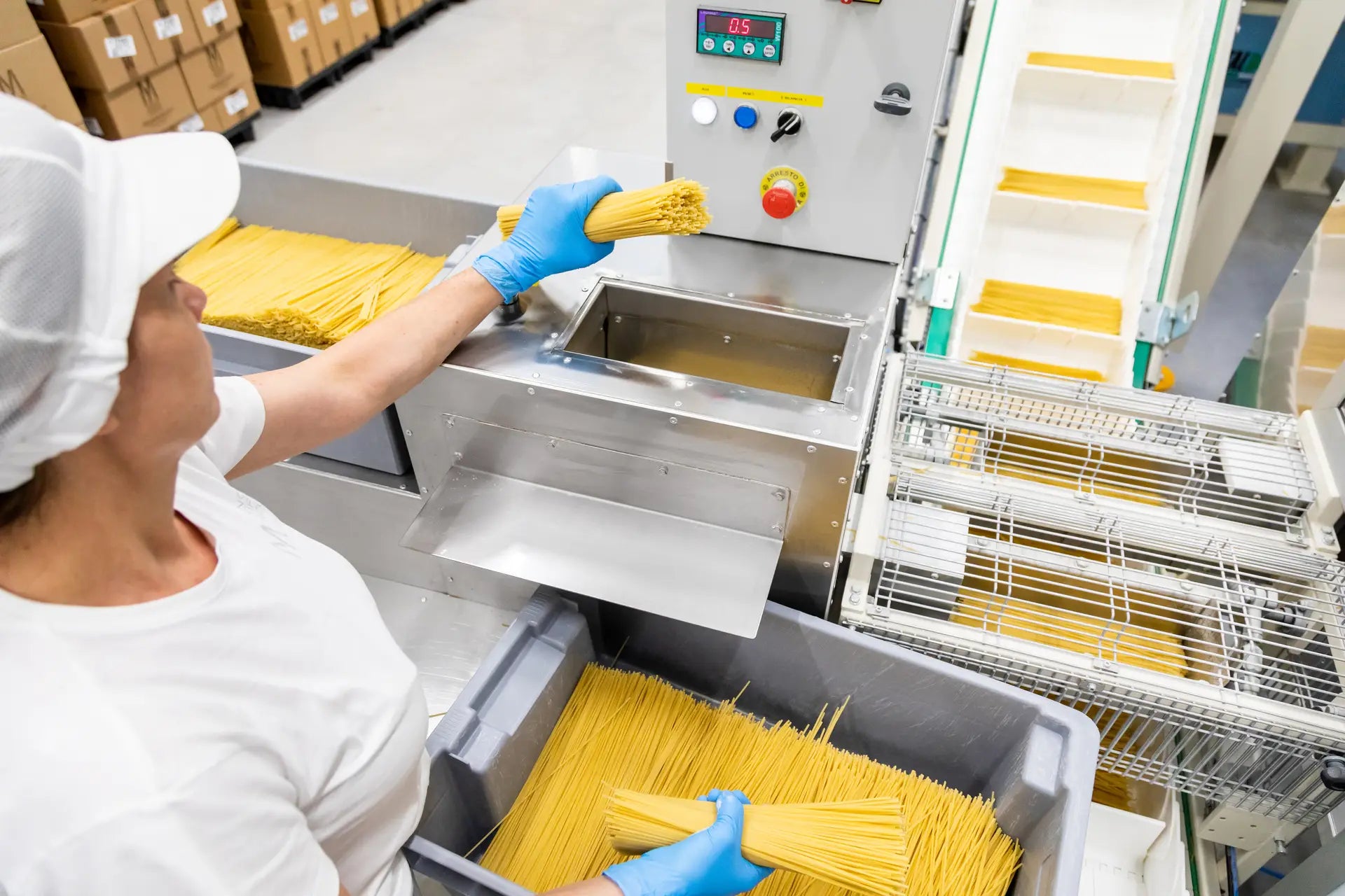 Mitarbeiterin legt 500 Gramm Mancini-Spaghetti in Maschine zur Sortierung.